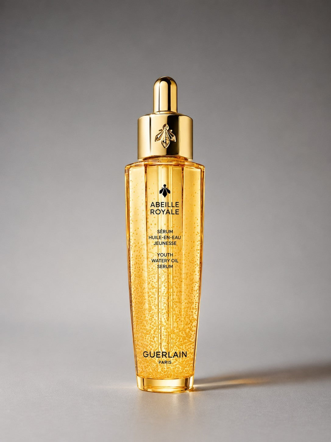 Flacon doré du sérum Abeille Royale de Guerlain, texture huile en eau avec bulles, bouchon doré orné d'une abeille.